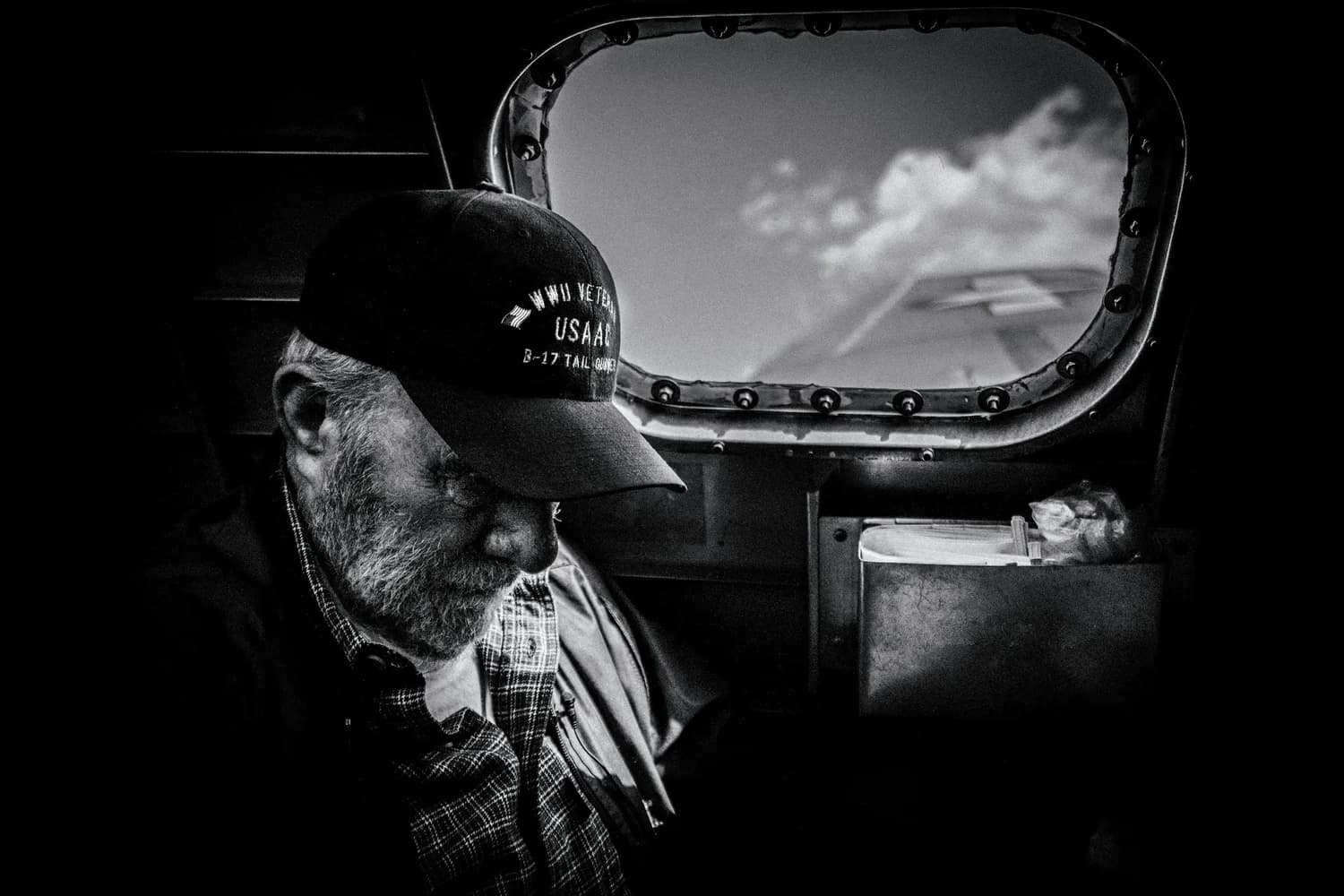 A veteran in a military cap looking out an aircraft window